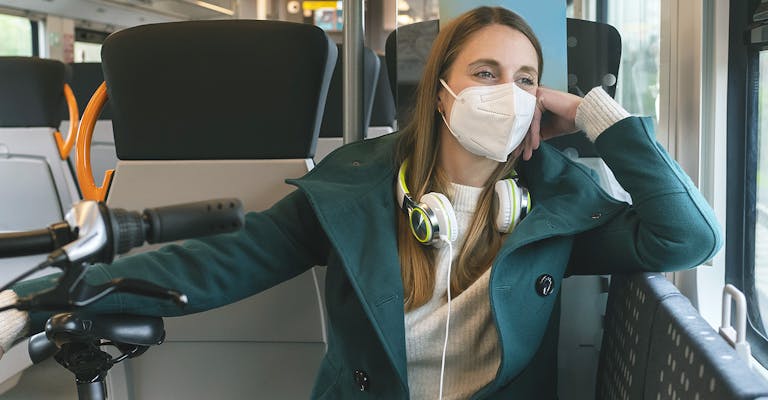 Photo d'une jeune fille qui regarde par une fenêtre d'un transport en commun type train. Elle à un vélo avec elle.