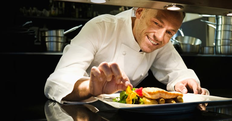 Photo d'un cuisinier souriant dans une cuisine de restaurant en train de placer sa touche finale à un plat dans une assiette