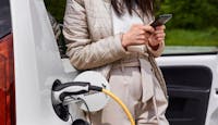 une femme recharge sa voiture électrique en consultant son smartphone 