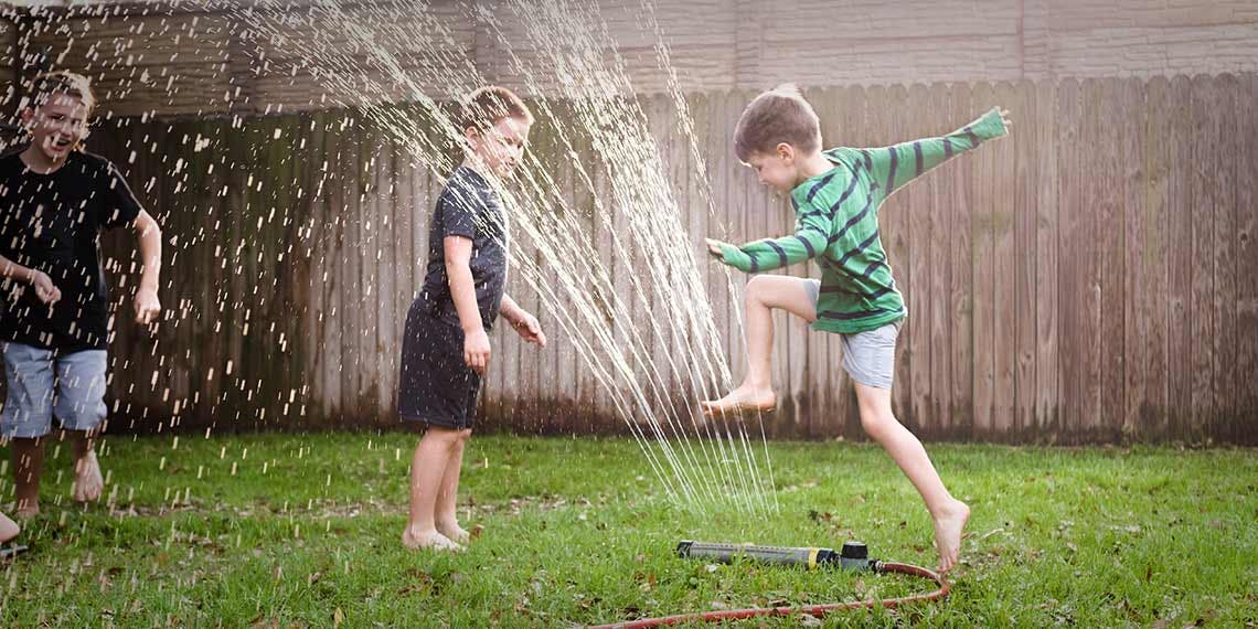 3 enfants jouent avec jet d'eau jardin

