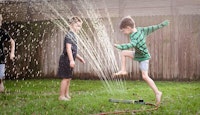 3 enfants jouent avec jet d'eau jardin
