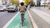 un jeune homme fait du vélo sur une piste cyclable en ville entouré de voitures 
