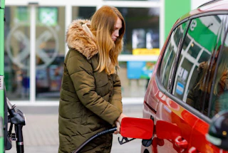 Une femme qui fait le plein de sa voiture rouge dans une station essence